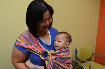 a mother holding her baby close in a cloth sling, both smiling
