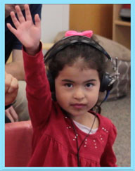 a girl wearing hearing screening equipment and raising her hand