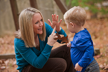 A woman signs to a young child holding an autumn leaf