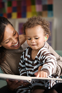 a mom reading with her young child, who is wearing a hearing aid